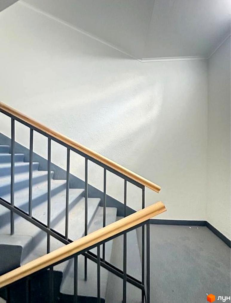 Сходи в житловому комплексі Героїв Маріуполя з дерев'яними поручнями та сірими стінами. Сучасний дизайн сходів та стін.