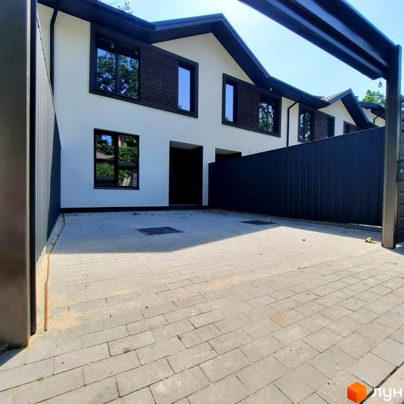 Таунхаус Т-37 з білим фасадом та темним дахом, з бруківкою на прибудинковій території. Комплекс розташований під відкритим небом.