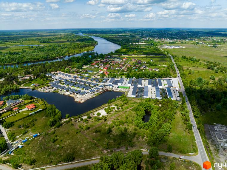 Панорамний вид на Котеджне містечко Prydesennya Eco Village з котеджами біля озера. Навколо зелені насадження та річка.