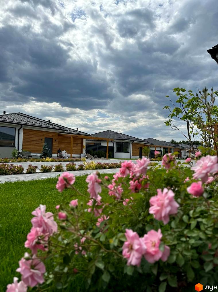 Вигляд котеджів у Котеджному містечку Prydesennya Eco Village з рожевими квітами на передньому плані та зеленою травою.