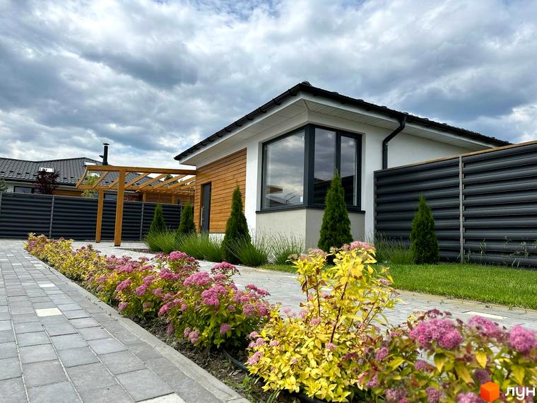 Вигляд будинку в Котеджному містечку Prydesennya Eco Village з озелененою прибудинковою територією та доріжкою з тротуарної плитки.