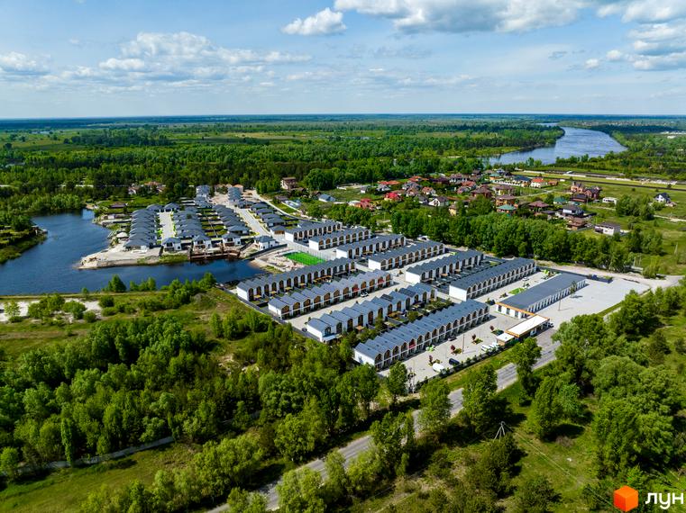 Вид з висоти на Котеджне містечко Prydesennya Eco Village з таунхаусами. Навколо будівель зелені насадження, річка та мальовничі краєвиди.