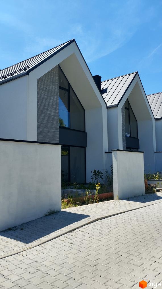 Зовнішній вигляд новобудови на вулиці Північна з білими стінами та сірим дахом. Прибудинкова територія вимощена плиткою.