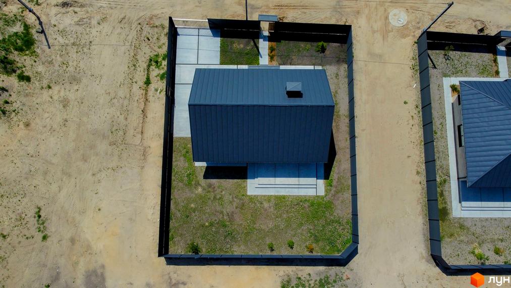 Котеджне містечко SMADE Park. Будинок з темним металевим дахом та сірими стінами, розташований на ділянці з газоном та бетонною доріжкою.