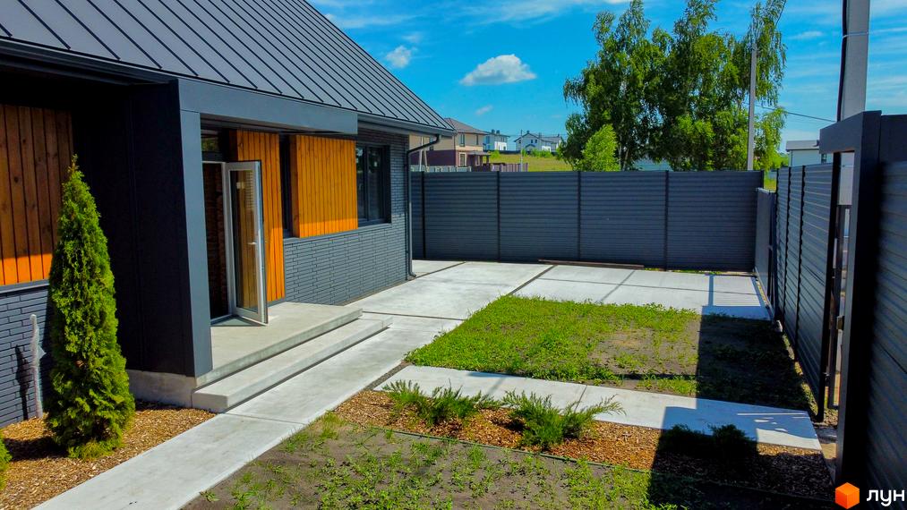 Котеджне містечко SMADE Park. Зовнішній вигляд будинку з сірого цегли та дерев'яними вставками, прибудинкова територія з бетонними доріжками та зеленню.