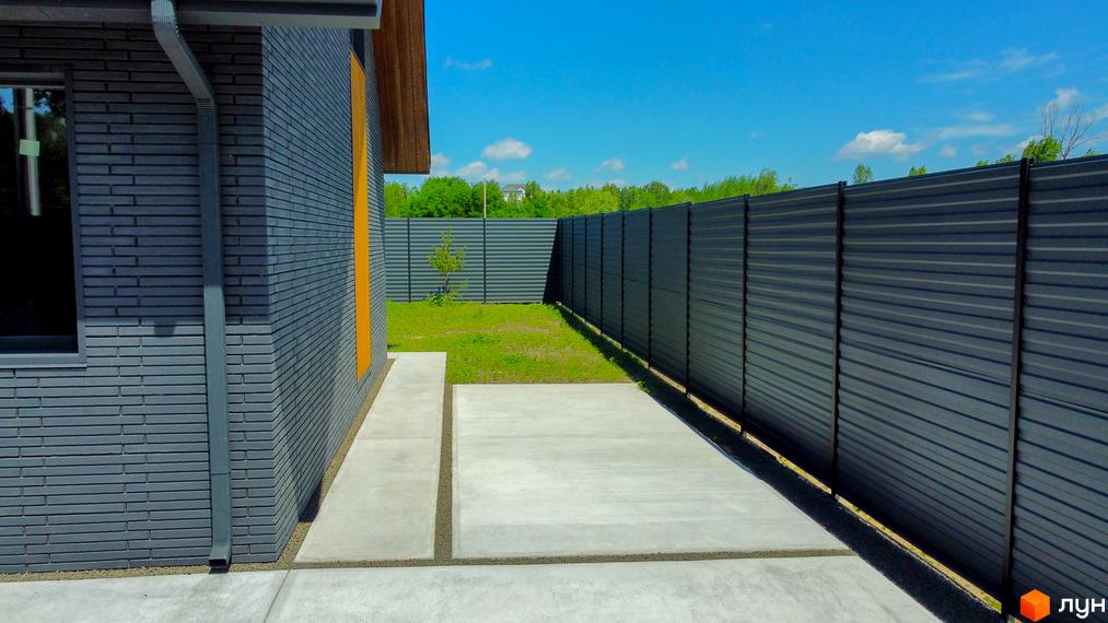 Зовнішній вигляд будинку з сірої цегли та бетонна доріжка біля будинку в КМ SMADE Park. Огороджена територія з металевим парканом.