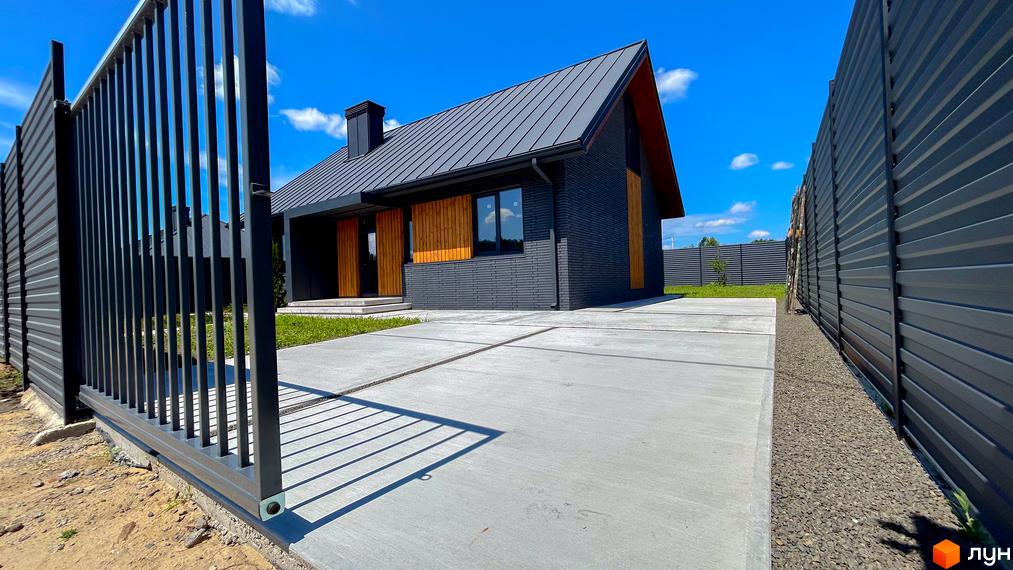 Котеджне містечко SMADE Park: сучасний будинок з темно-сірої цегли та металевим дахом, прибудинкова територія з бетонною доріжкою та огорожею.