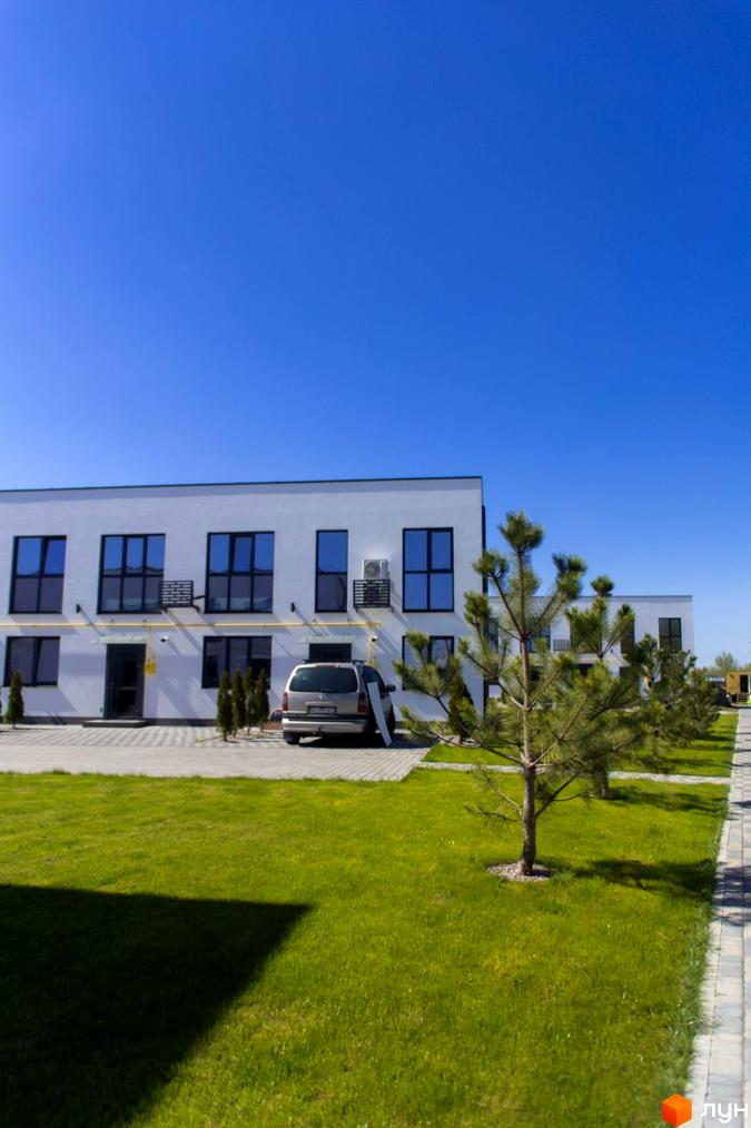 Зовнішній вигляд таунхаусів DREAM HOUSE з великими вікнами та кондиціонерами. Прибудинкова територія з газоном, деревами та вимощеною доріжкою.