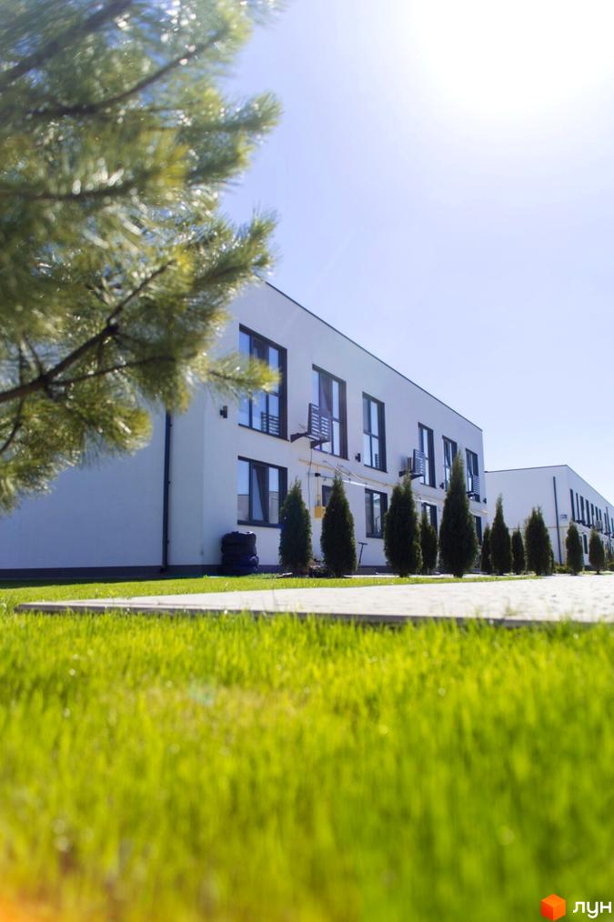 Таунхауси DREAM HOUSE: білі двоповерхові будинки з темними вікнами, оточені зеленим газоном та рядами невеликих дерев.