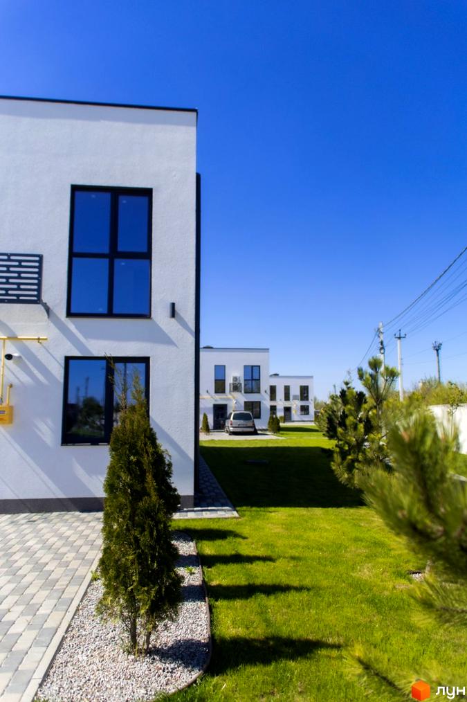 Таунхауси DREAM HOUSE - білі двоповерхові будинки з темними вікнами та доглянутою зеленою територією. Поруч розташовані інші новобудови комплексу.