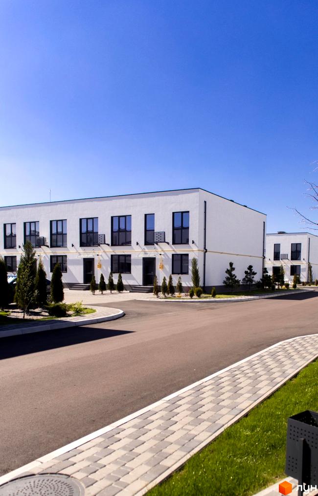 Фасад житлового комплексу DREAM HOUSE з білими стінами та чорними вікнами. Прибудинкова територія з доглянутим газоном та бруківкою.