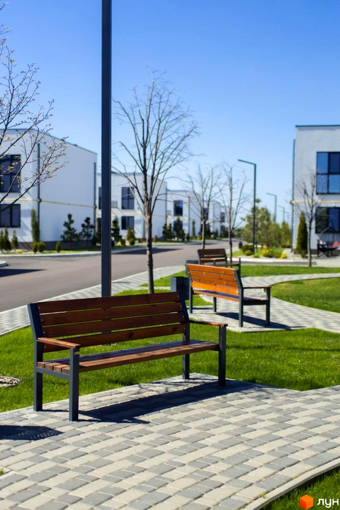 Таунхауси DREAM HOUSE з дерев'яними лавками та доглянутою зеленою зоною. Сучасна архітектура будинків та брукована доріжка.