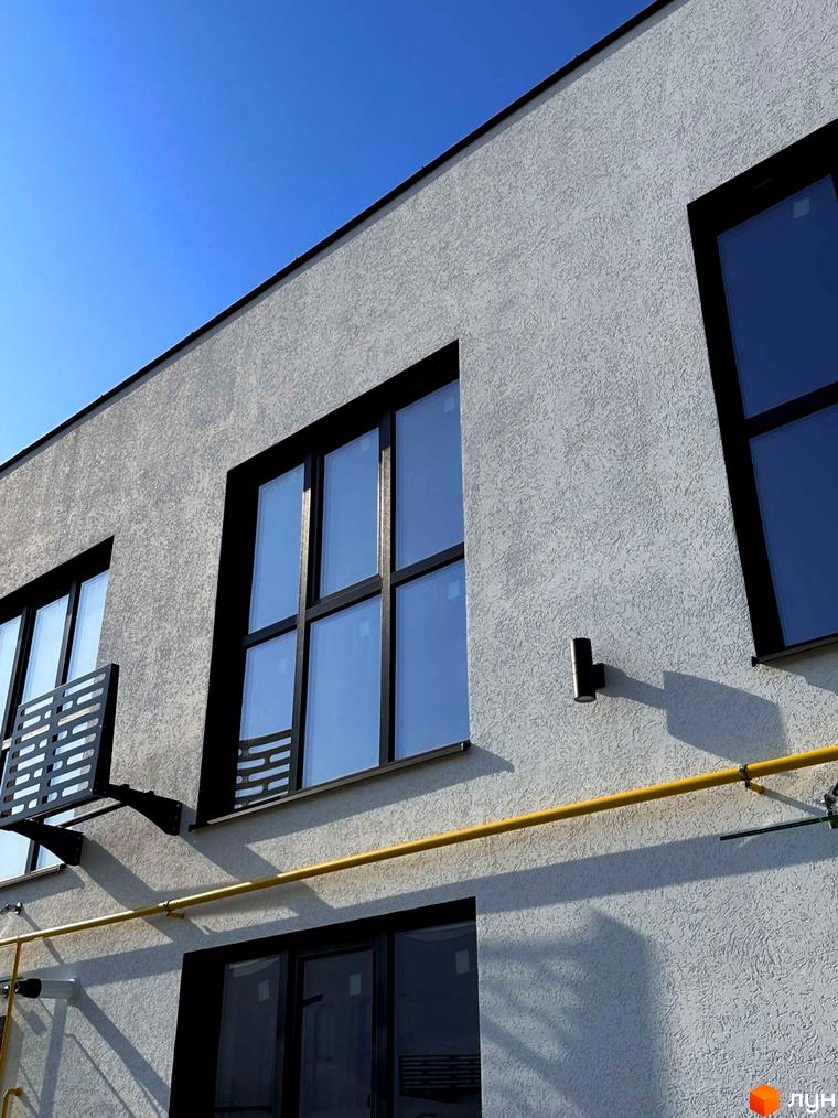 Зовнішній вигляд Таунхаусів DREAM HOUSE: світлий фасад з текстурною штукатуркою, чорні віконні рами та жовта газова труба.