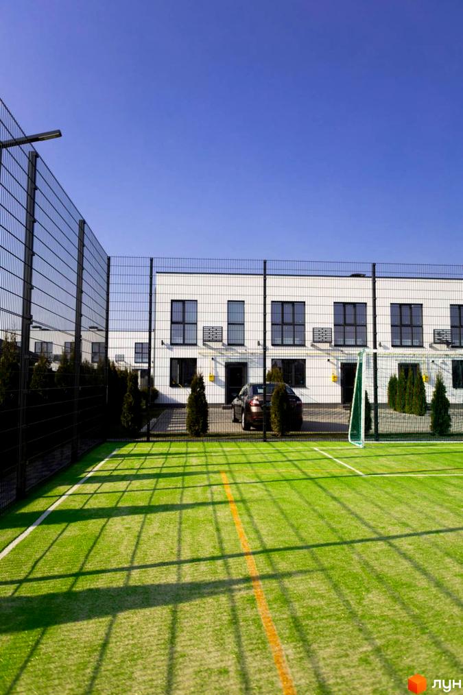 Зовнішній вигляд таунхаусів DREAM HOUSE з великими вікнами та прибудинковою територією, що включає спортивний майданчик та зелені насадження.