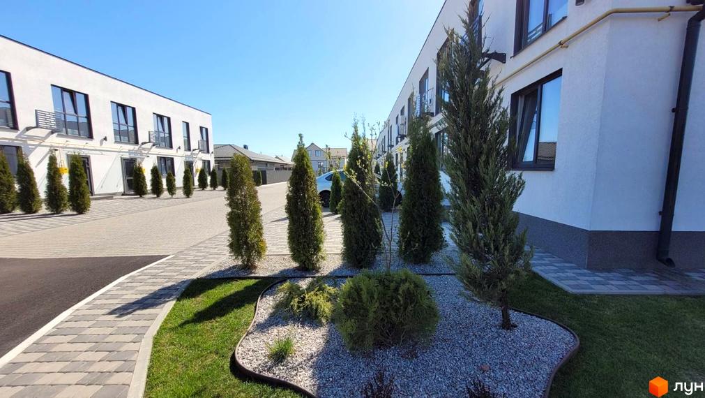 Таунхауси DREAM HOUSE з білими фасадами та темними вікнами, розташовані на доглянутій прибудинковій території з туями та газоном.