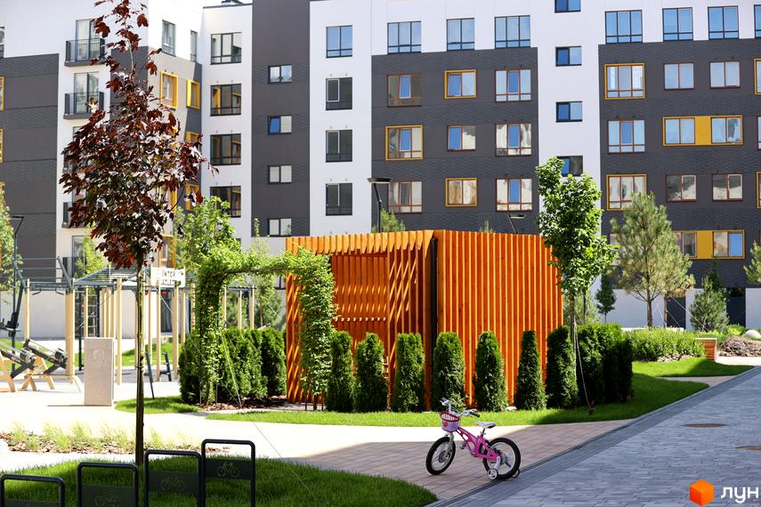 Житловий комплекс Молодість: фасади будинків з різнокольоровими вікнами та зелена прибудинкова територія зі спортивним майданчиком та дитячим велосипедом.
