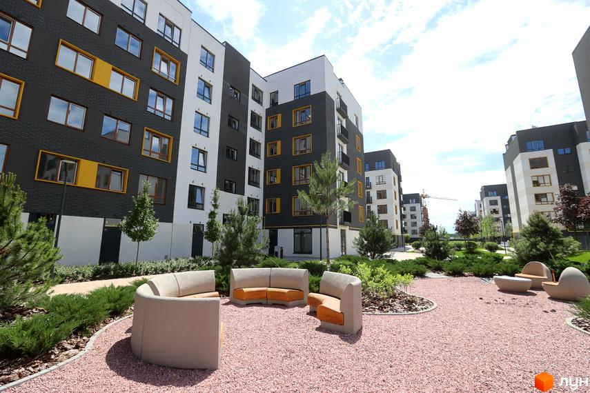 Житловий комплекс Молодість: фасади будинків з чорними та білими секціями, жовтими вікнами, та зелена прибудинкова територія з місцями для відпочинку.