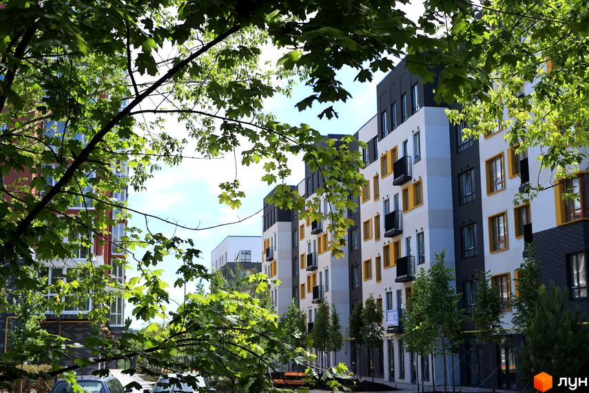 Зовнішній вигляд новобудови ЖК Молодість з білими та сірими фасадами, жовтими вікнами та балконами, оточений зеленню та деревами.