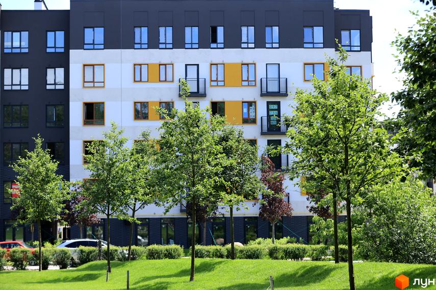 Зовнішній вигляд будинку ЖК Молодість з білими та жовтими елементами фасаду, вікнами та балконами. На прибудинковій території зелена галявина та дерева.