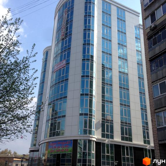 Зовнішній вигляд новобудови ЖК Атлантіс з панорамними вікнами та білим фасадом. Поруч видно дерева та сусідні будівлі.