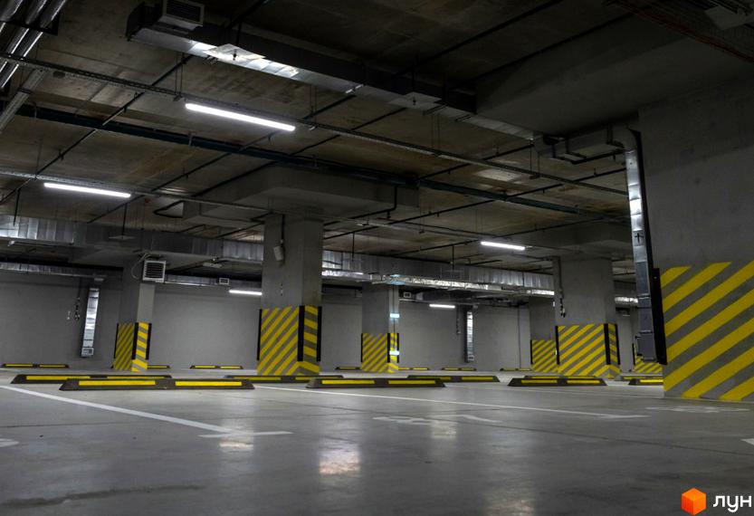 Паркінг в новобудові ЖК Sense City. Бетонні колони з жовто-чорною розміткою, паркувальні обмежувачі та яскраве освітлення.