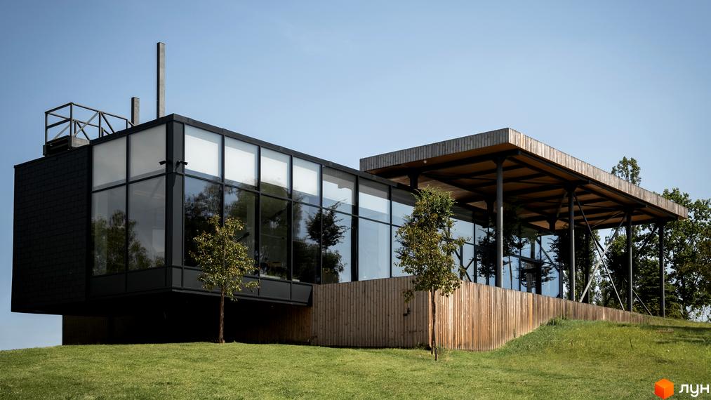 Сучасна двоповерхова будівля з панорамними вікнами та дерев'яною терасою, оточена зеленою галявиною та деревами. Vlasne Misto.