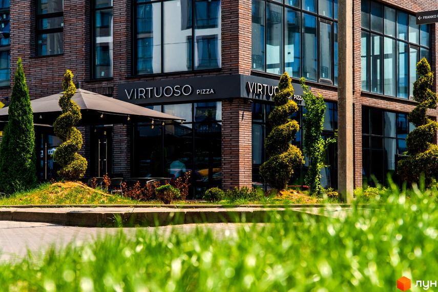 Зовнішній вигляд будівлі Virtuoso Pizza в Житловому комплексі Паркова Алея. Навколо будівлі зелені насадження та доглянута територія.
