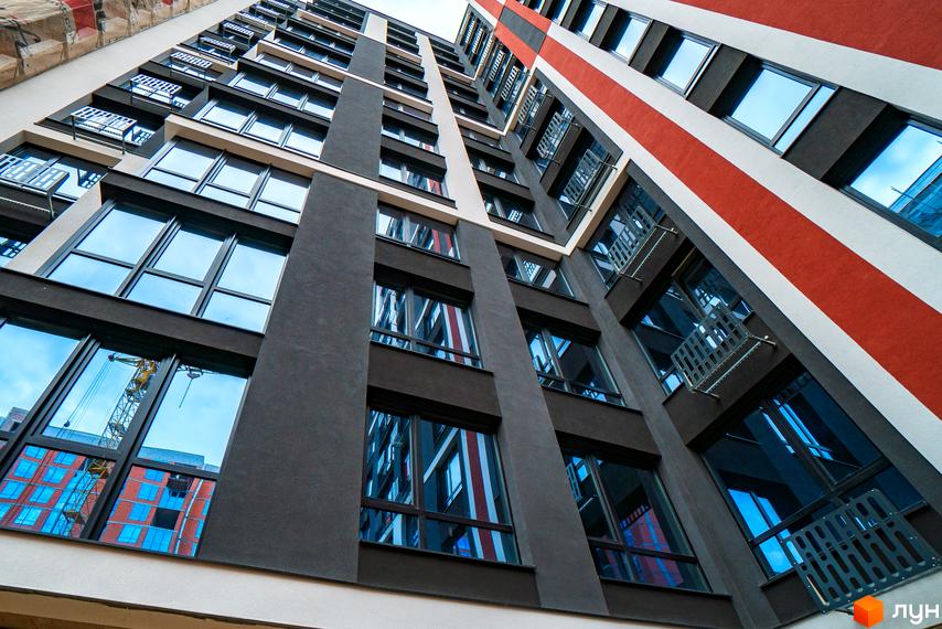 Висотна будівля ЖК U One з великими вікнами та балконами. Фасад будинку пофарбовано у темні кольори з червоними смугами.