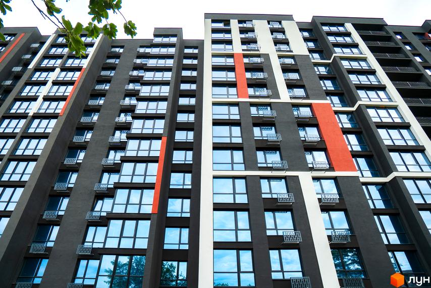 Висотна будівля ЖК U One з великими вікнами, балконами та яскравими акцентами на фасаді.  Навколо будинку зелені дерева та блакитне небо.