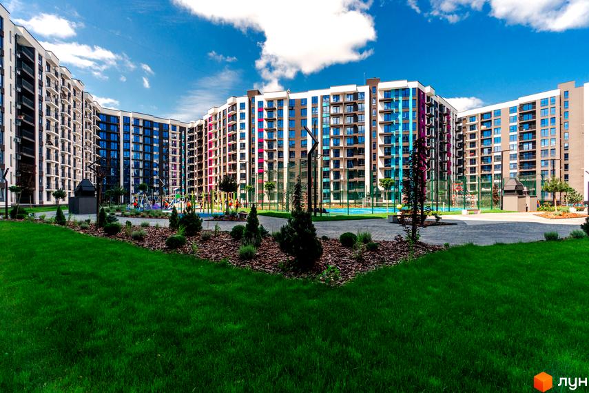 Зображення фасаду Новобудови Family Plaza з великими вікнами та прибудинковою територією з газоном.