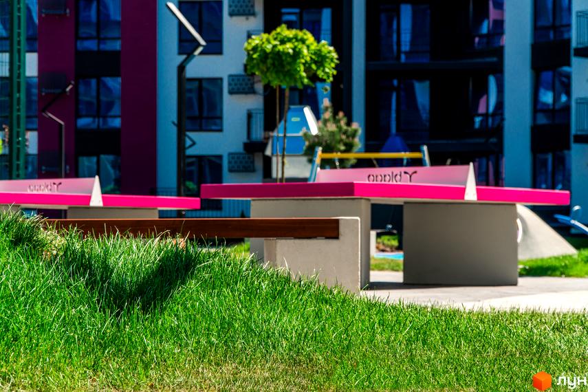 Житловий комплекс Family Plaza з рожевими тенісними столами на зеленій території. Вигляд на будівлі з вікнами.