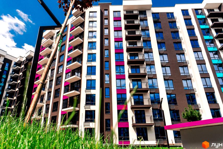 Зовнішній вигляд багатоповерхового будинку в Житловому комплексі Family Plaza з балконами та великими вікнами. На передньому плані зелена трава.