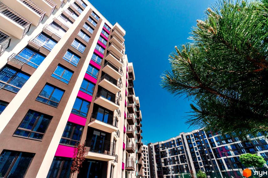 Зображення фасаду будинку Житлового комплексу Family Plaza з балконами та вікнами. Навколо будівлі зелені насадження та блакитне небо.