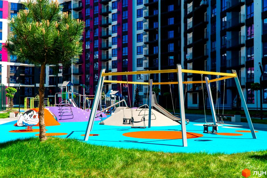 Зображення дитячого майданчика з гірками та гойдалками на території Житлового комплексу Family Plaza. Багатоповерховий будинок на задньому плані.