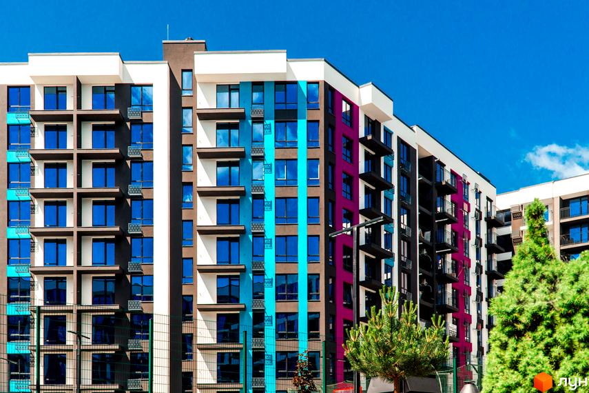 Зовнішній вигляд ЖК Family Plaza з кольоровими фасадами та великими вікнами. На передньому плані зелені насадження.