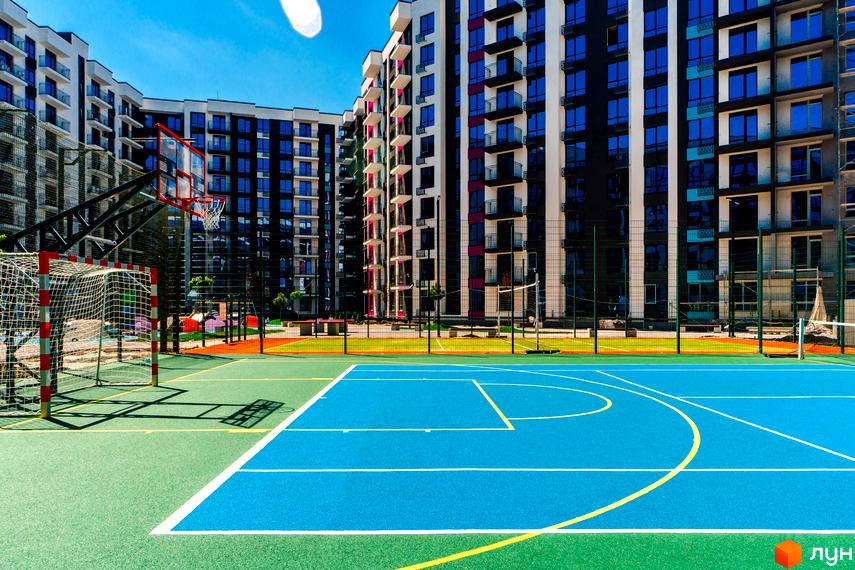 Зображення ігрового майданчика біля багатоповерхового будинку в Житловому комплексі Family Plaza. На задньому плані висотні будинки з балконами.