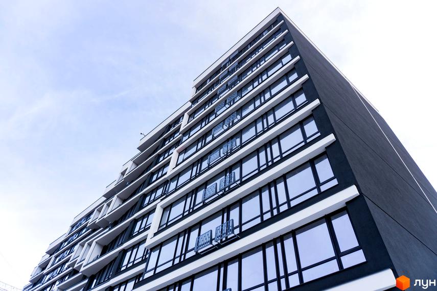 Фасад житлового комплексу А5 з великими вікнами та балконами. Зовнішній вигляд новобудови з сірим фасадом та білими елементами.