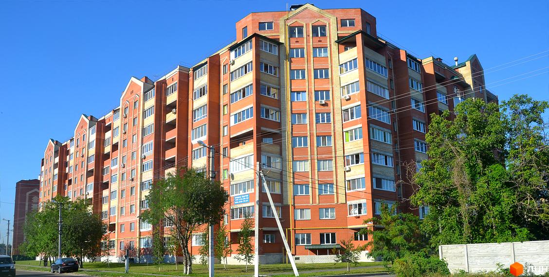 Житловий комплекс Левада - це цегляна багатоповерхівка з численними вікнами та балконами, розташована на фоні ясного блакитного неба. Навколо будівлі зелені дерева та доглянута прибудинкова територія.