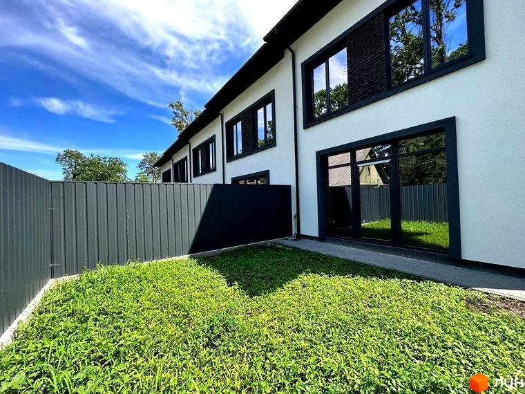 Зовнішній вигляд таунхауса T-35 з великими вікнами та зеленим газоном перед будинком. Видно частину огорожі.