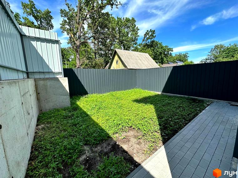 Таунхаус Т-35 з сірим дахом. Прилегла територія має зелений газон, вимощену доріжку та високі паркани.