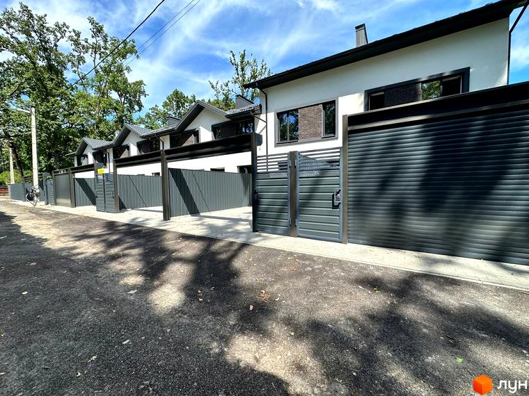 Таунхаус Т-37 – двоповерховий будинок з сірим парканом та воротами. Навколо будинку облаштована прибудинкова територія з бруківкою та деревами.