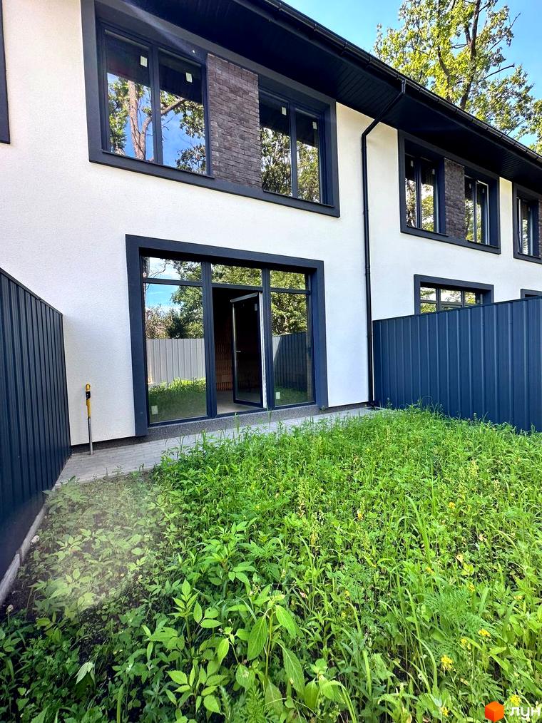 Таунхаус Т-37 – двоповерховий будинок з великими вікнами та цегляними вставками, прибудинкова територія з зеленою травою та парканом.