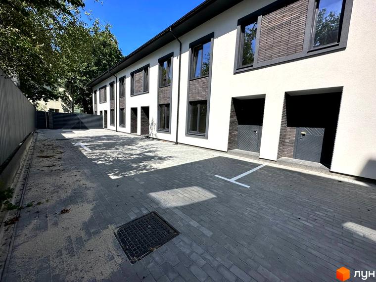 Зовнішній вигляд будинку на Ярославській, 26в. На фото прибудинкова територія з парковкою та тротуаром.