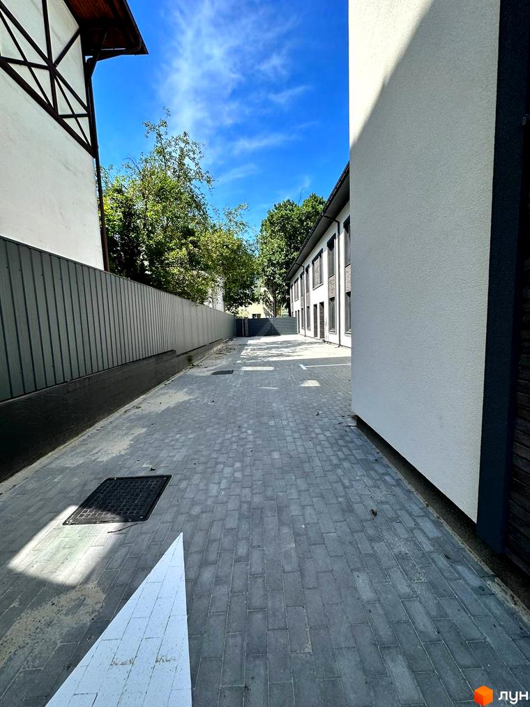 Фото фасаду будинку по вул. Ярославська, 26в. Вид на пішохідну зону з тротуарною плиткою та металевим парканом.