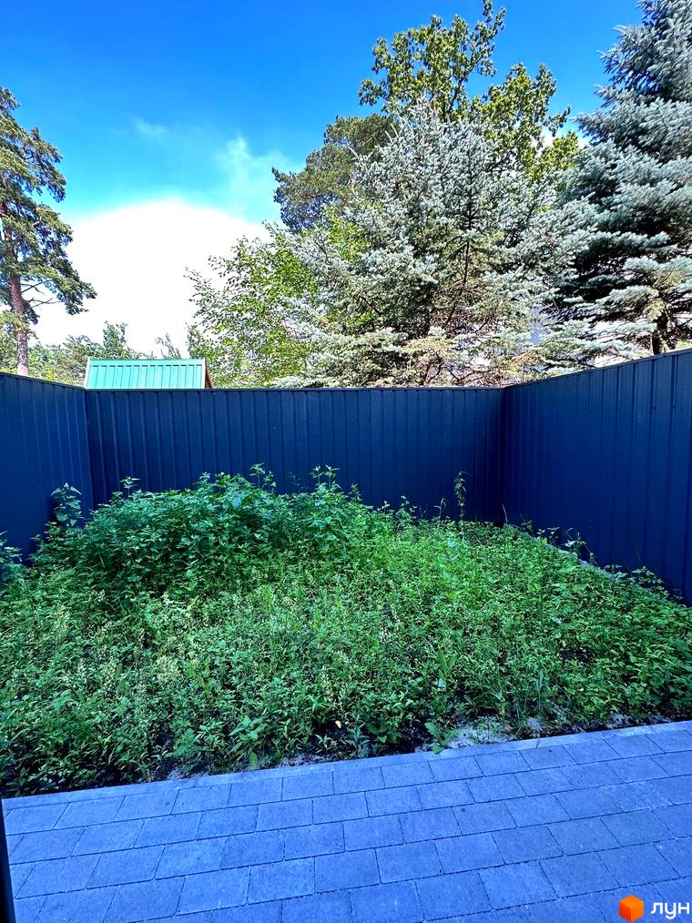 Новобудова на вулиці Ярославська, 26в, з густими зеленими насадженнями та синім металевим парканом на прибудинковій території.
