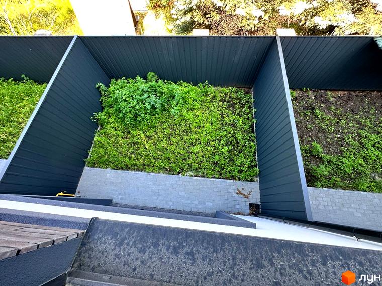 Зовнішній вигляд житлового комплексу на вул. Ярославська, 26в з зеленими насадженнями та сірими стінами. Прибудинкова територія з рослинністю та ґрунтом.