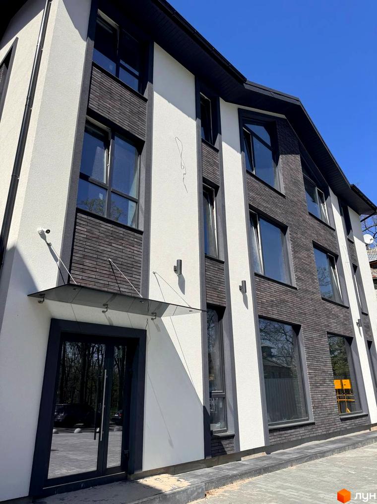 Зображення фасаду будинку на Ярославській, 26в. Багатоповерхова будівля з великими вікнами та оздобленням з цегли.