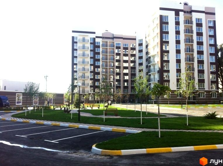 Зовнішній вигляд багатоповерхових будинків ЖК Центральний з балконами та вікнами. Прибудинкова територія з парковкою, зеленими насадженнями та лавками.