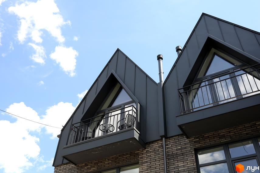 AMA FAMILY RESORT: сучасна архітектура житлового комплексу з темним фасадом та балконами на тлі блакитного неба з хмарами.