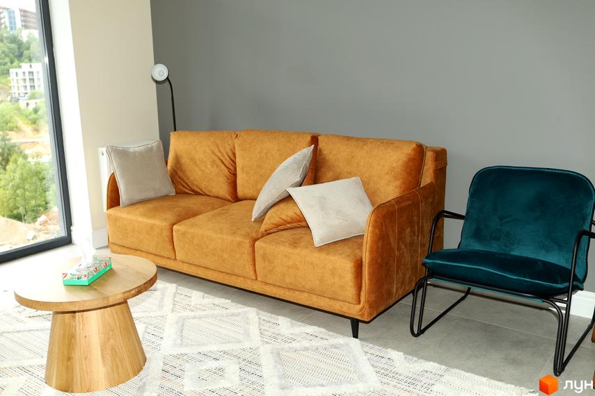 Інтер'єр вітальні з помаранчевим диваном та бірюзовим кріслом. Навколо дивана розташовані подушки, а поруч стоїть дерев'яний журнальний столик.